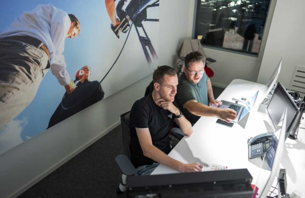 Twee mannen op de redactie van omroep Venlo kijken geïnteresseerd naar een computerscherm
