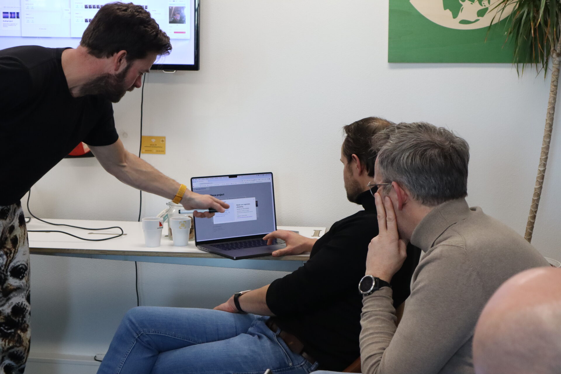Drie mannen kijken naar een laptop tijdens een workshop van het coachingstraject.