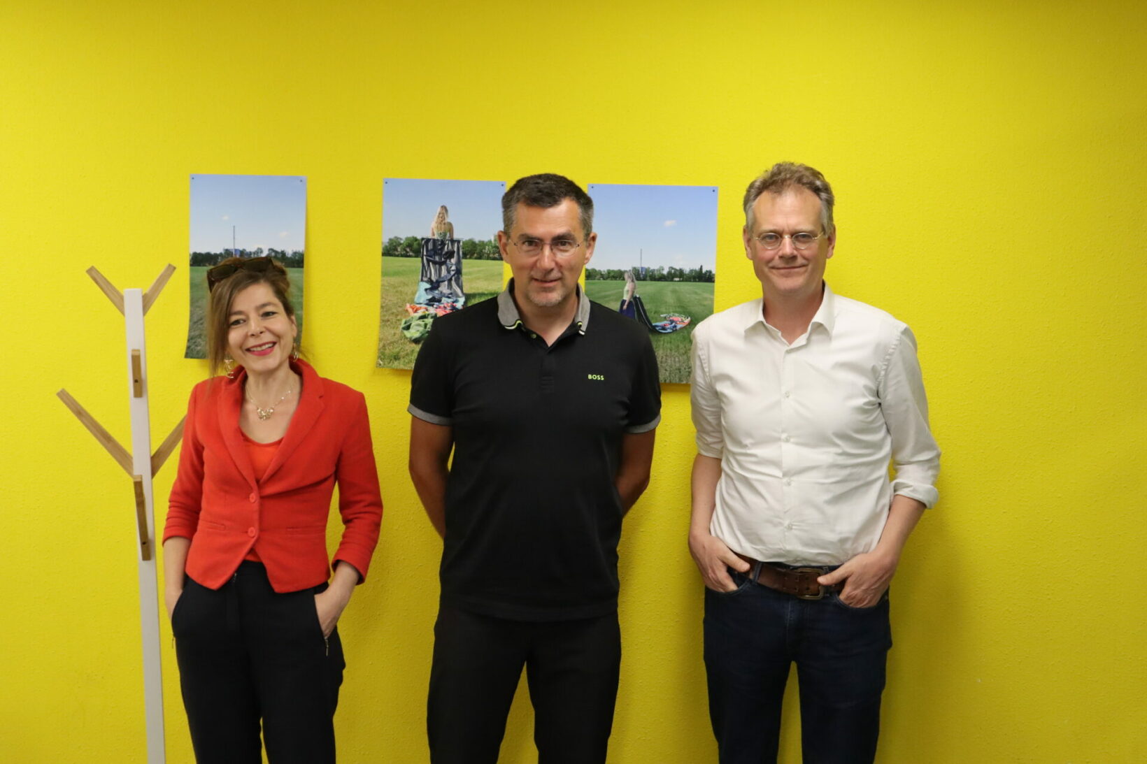 Het team van The Content Exchange bestaande uit drie personen voor een gele muur.