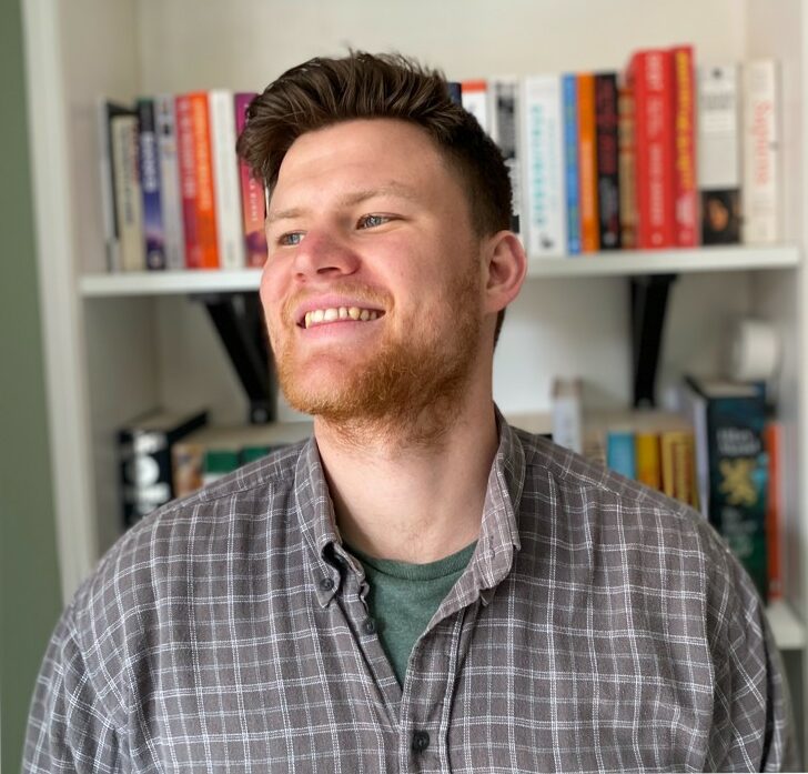 Portretfoto Paul Dobson. Hij draagt een geruit overhemd en staat voor een boekenkast.