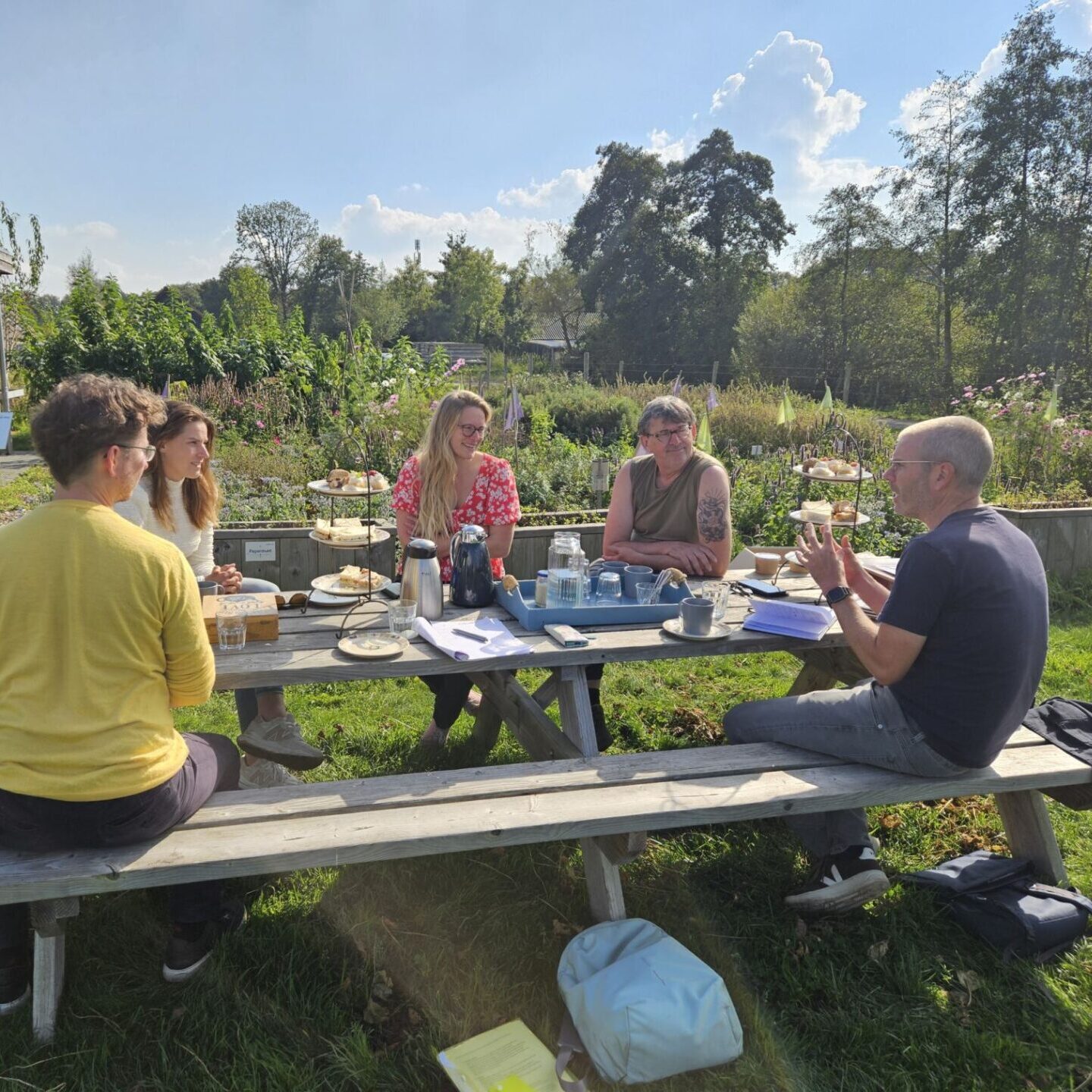 Tijdens een bijeenkomst van Incubator team Circulaire Journalistiek zitten enkele personen op een zonnige dag buiten aan een picknicktafel te overleggen.